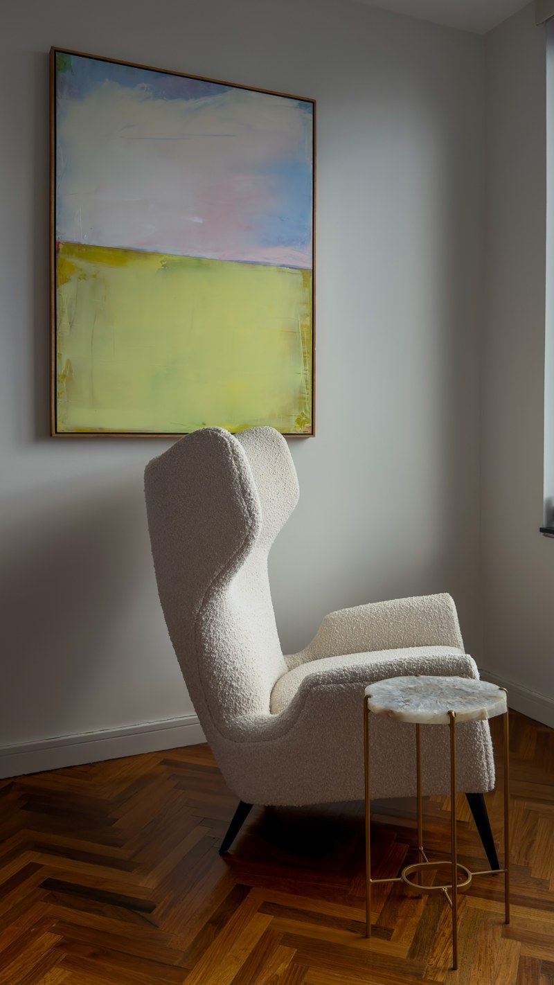 A white wing chair beneath abstract art